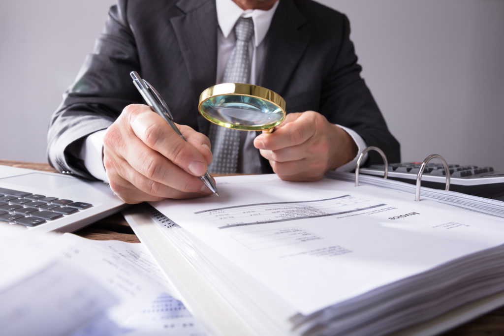 Close-up,Of,A,Businessperson's,Hand,Looking,At,Receipts,Through,Magnifying